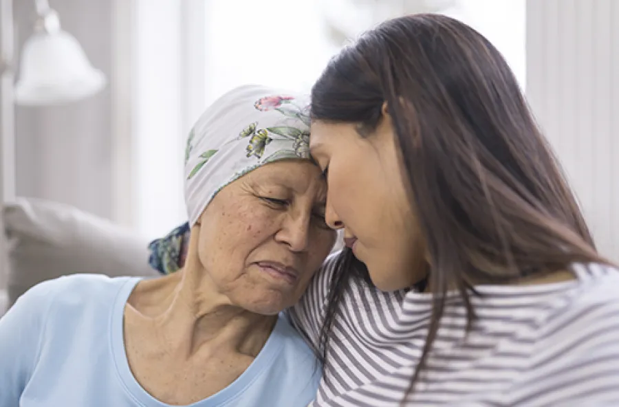 Elderly woman wearing headscarf and younger woman share a tender moment of support and comfort indoors