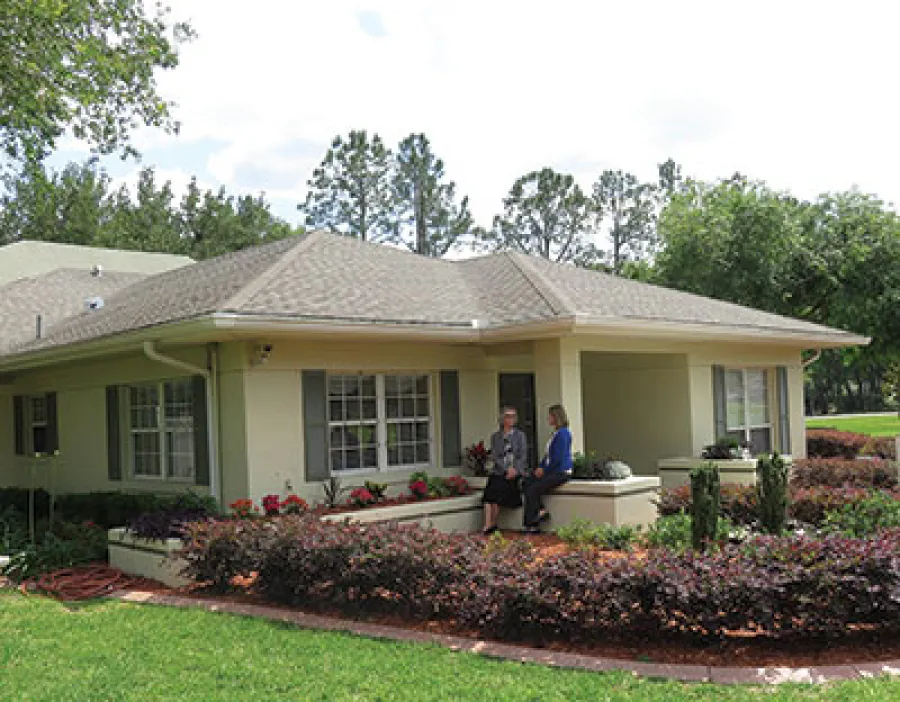 Single-story house with beige walls, large windows, and landscaped garden with shrubs and flowers