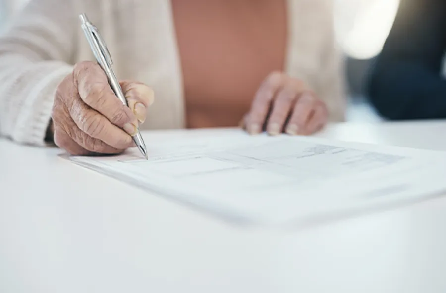 Close-up of a person writing with a pen on printed documents on a white table