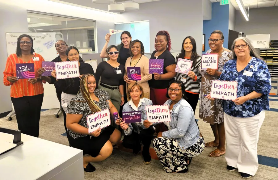 Diverse group of people in office holding signs with messages of empathy, unity, and love in a bright workspace.