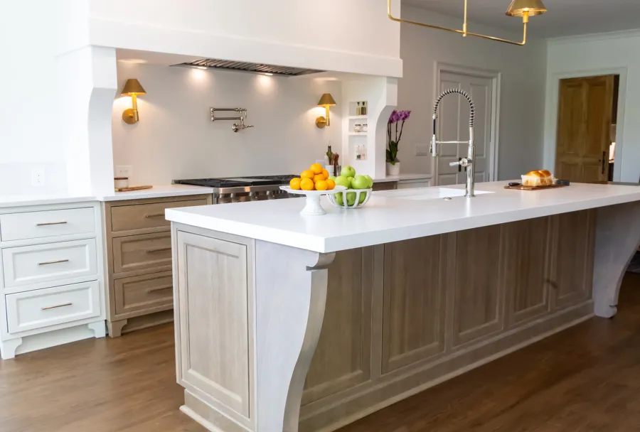 Modern kitchen with large wooden island, white countertop, stainless steel faucet, and fruit bowls with oranges and apples