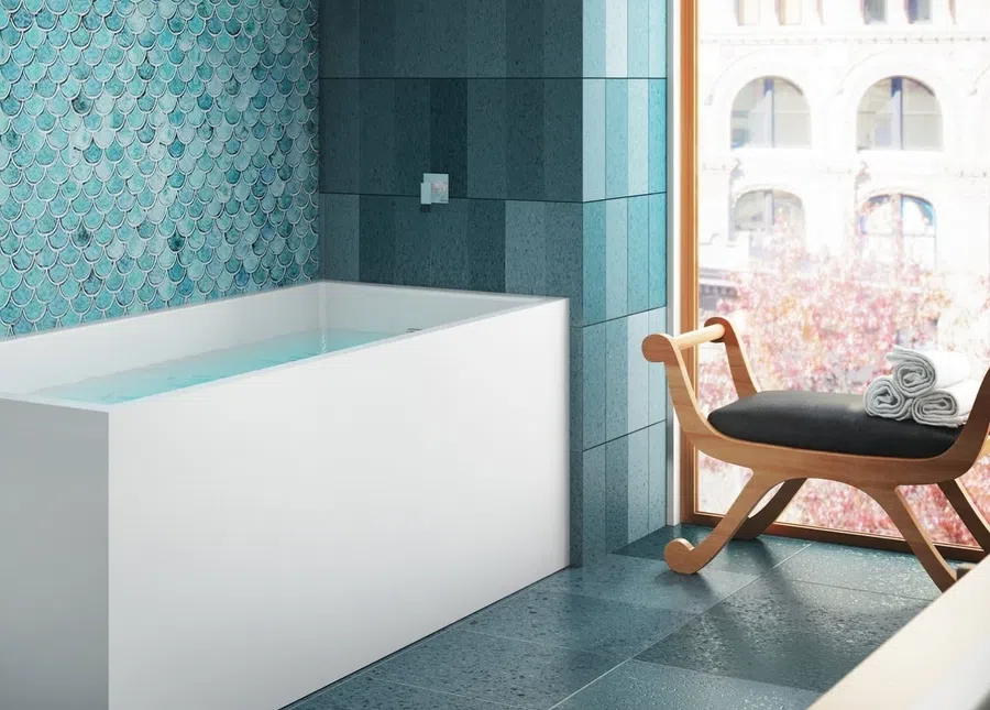 Modern bathroom with a white bathtub, blue tiled walls, and a wooden chair by a large window.
