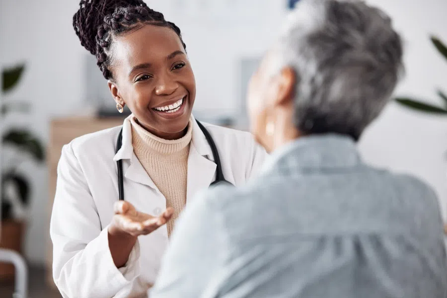 Female doctor with stethoscope smiling and talking to elderly patient in a medical office setting.