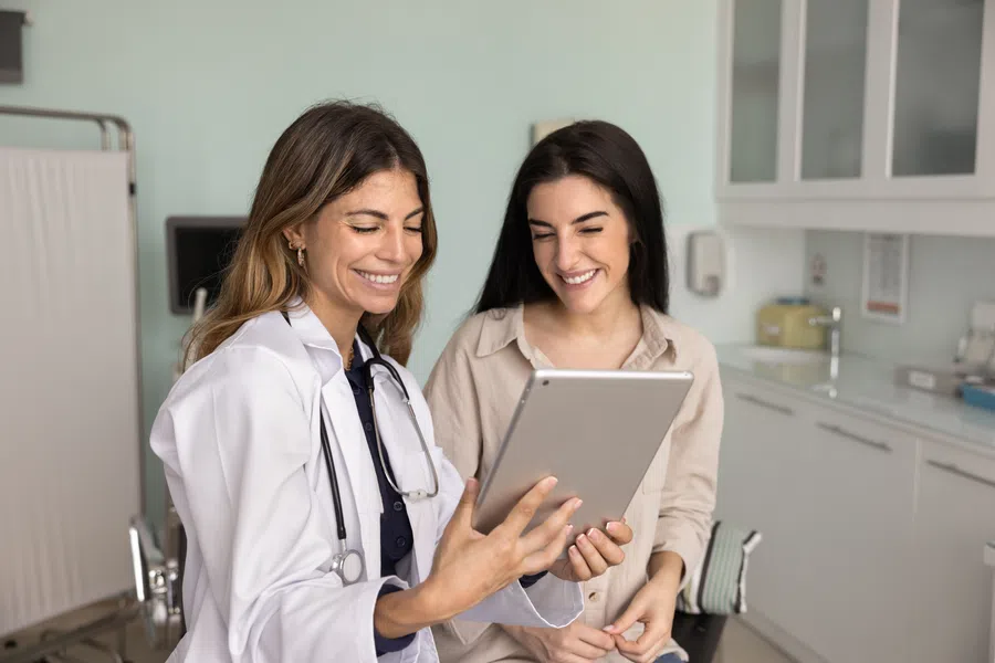 Female doctor showing medical information on tablet to a smiling patient in a clinic room