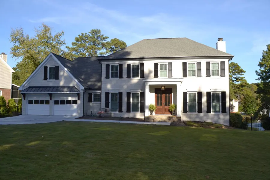 Two-story white house with black shutters, double garage, wooden front door, and large front lawn under clear sky