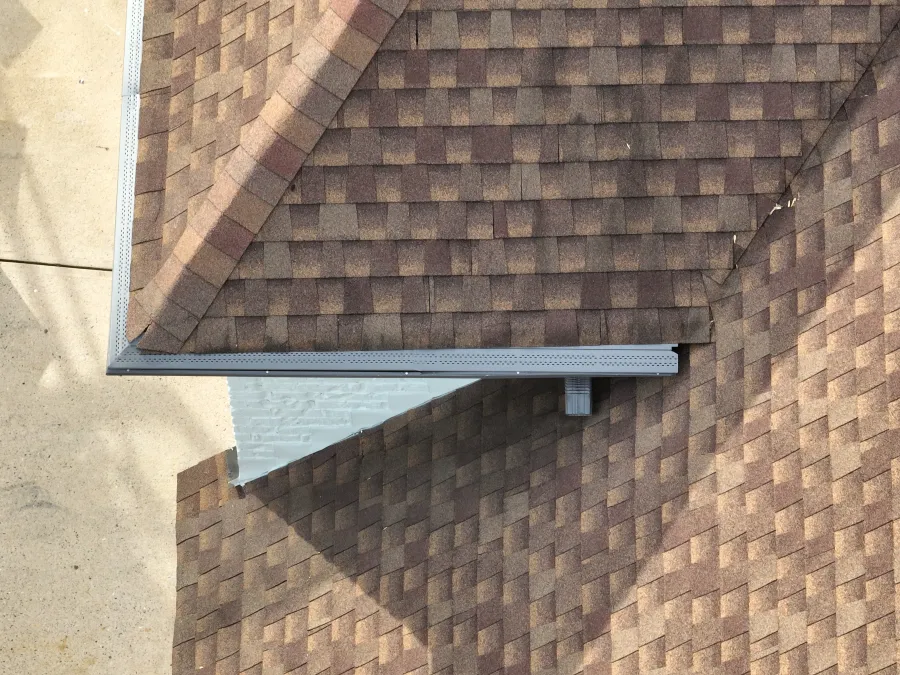Aerial view of intersecting brown shingle roofs with gutter system and concrete driveway.