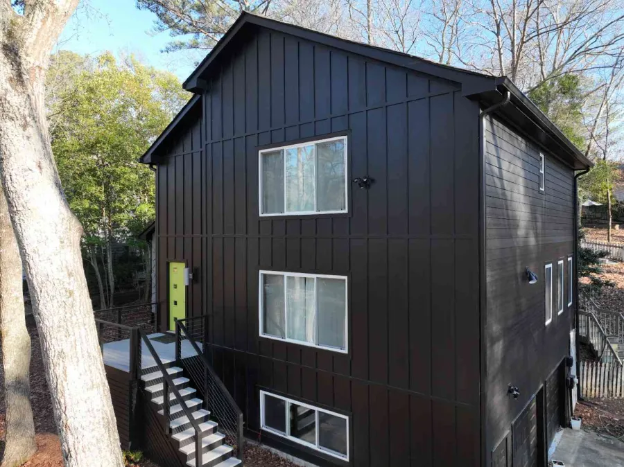 Modern three-story black house with large windows and yellow door surrounded by trees and outdoor stairs.