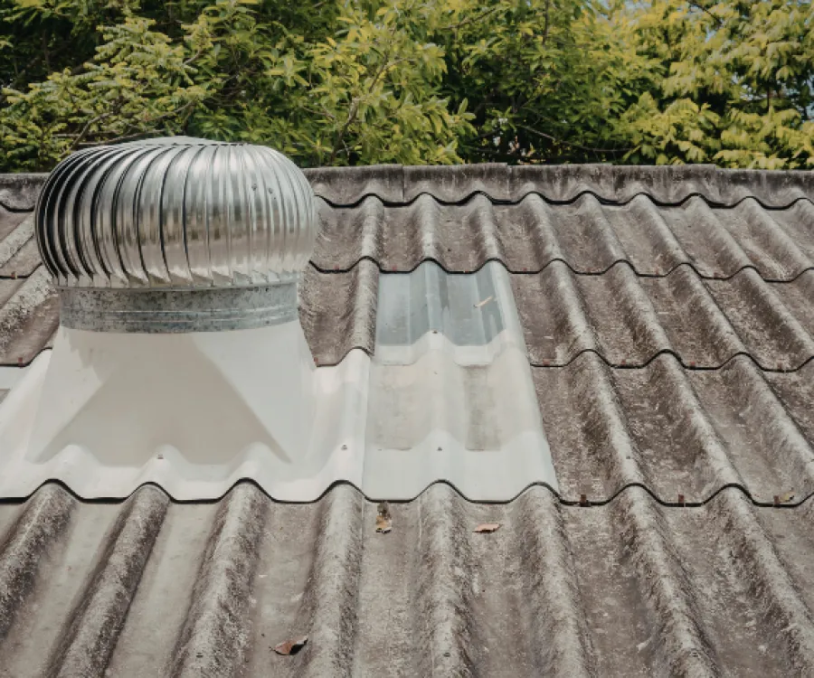 Silver roof turbine vent on a dirty corrugated metal roof with green trees in background.