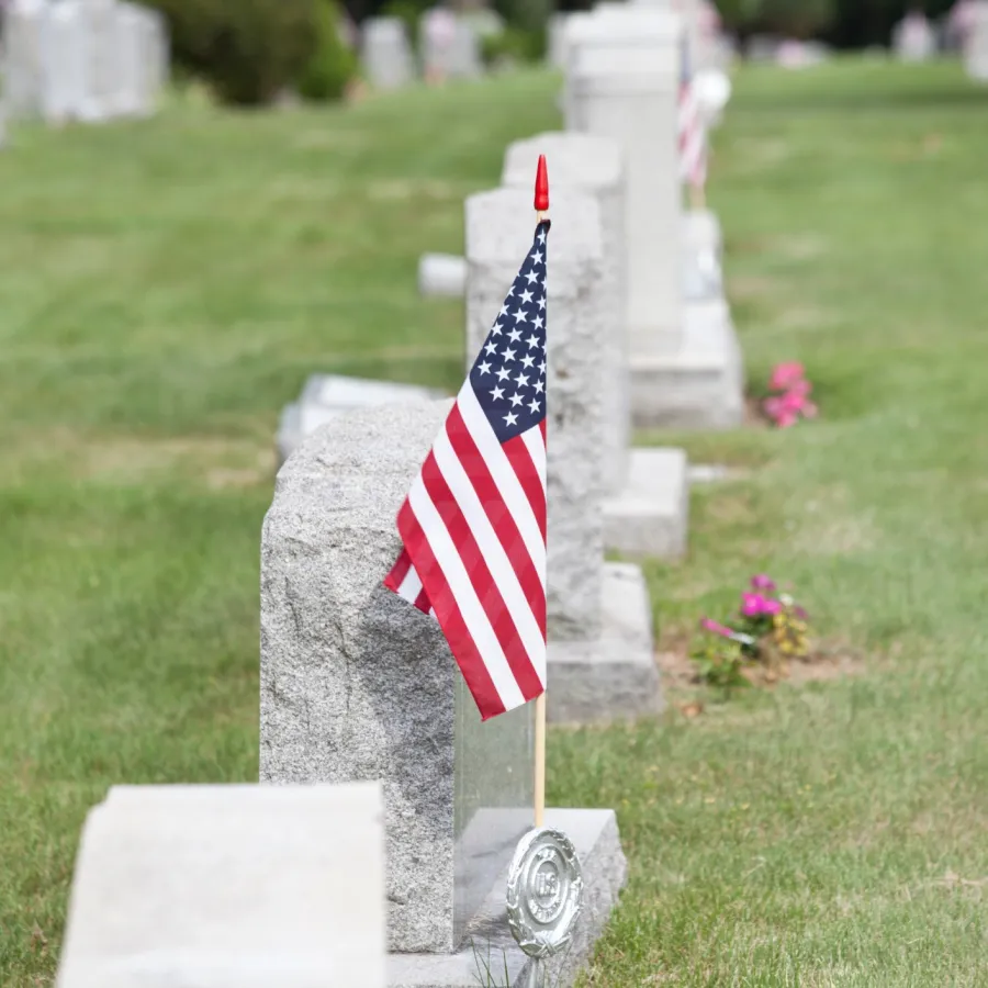 American flag placed on a gravestone in a cemetery with rows of headstones and green grass