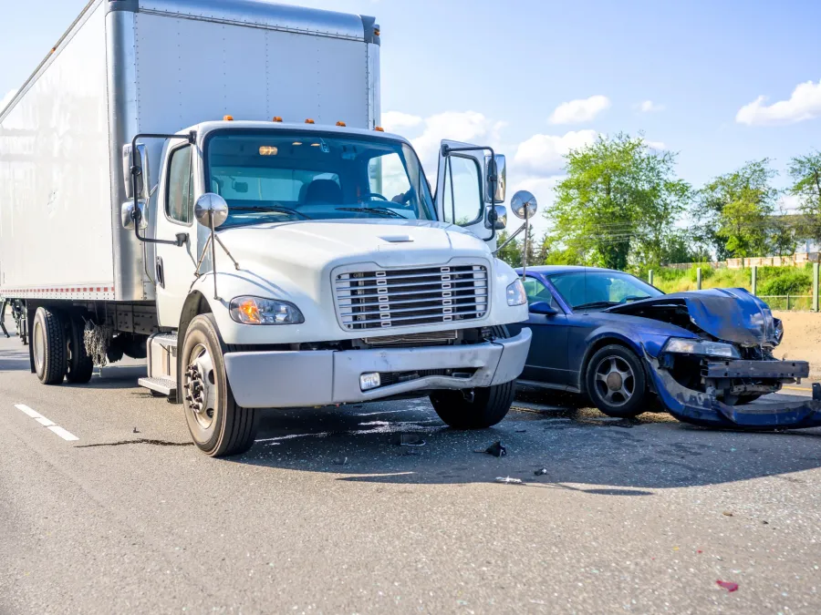 White box truck and blue sedan with front-end damage after a collision on a sunny highway.