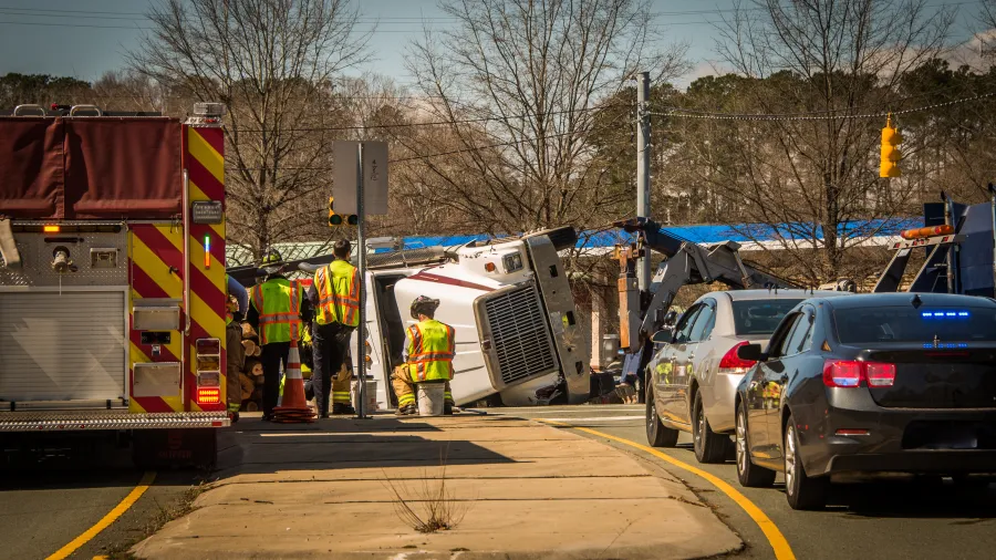 Emergency responders at the scene of an overturned truck on a road near police and fire vehicles