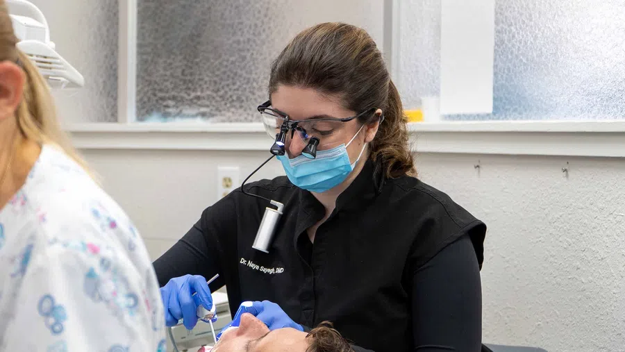 Dentist wearing magnifying glasses and mask performing dental procedure on patient in clinic.