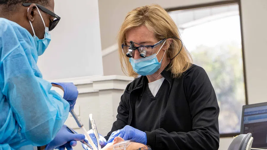 Dentists wearing masks and gloves performing a dental procedure using precision instruments in a clinical setting.