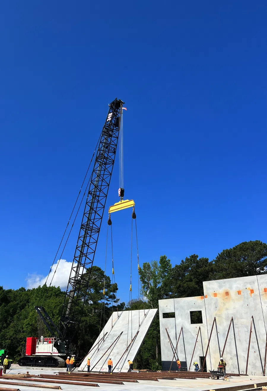 Construction site with a crane lifting large concrete panels under a clear blue sky.