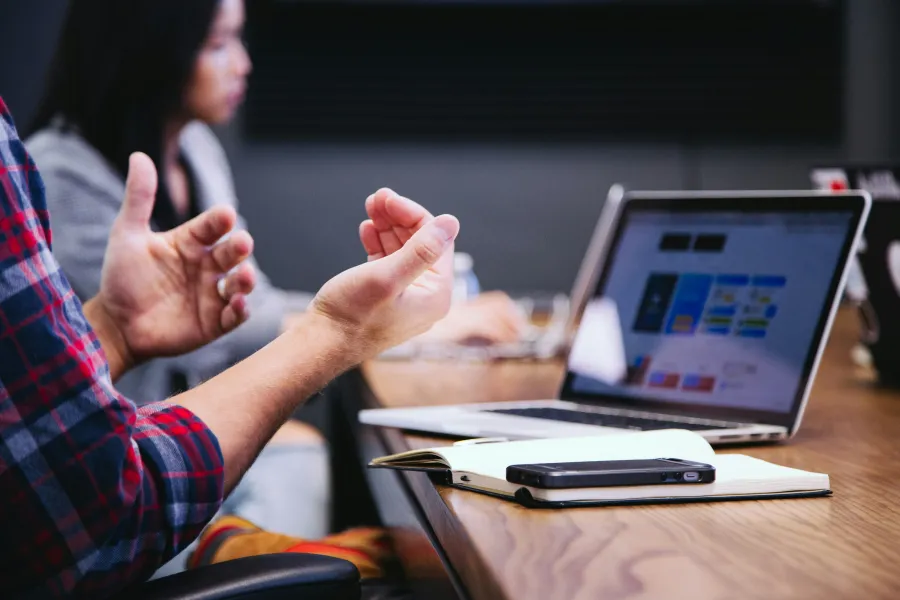 Person gesturing during a laptop meeting with notebook and smartphone on the table in a conference room