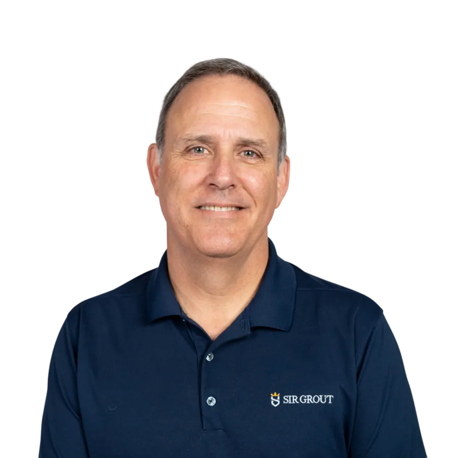 Man wearing navy blue Sir Grout polo shirt and beige pants smiling with hands resting on lap against transparent background