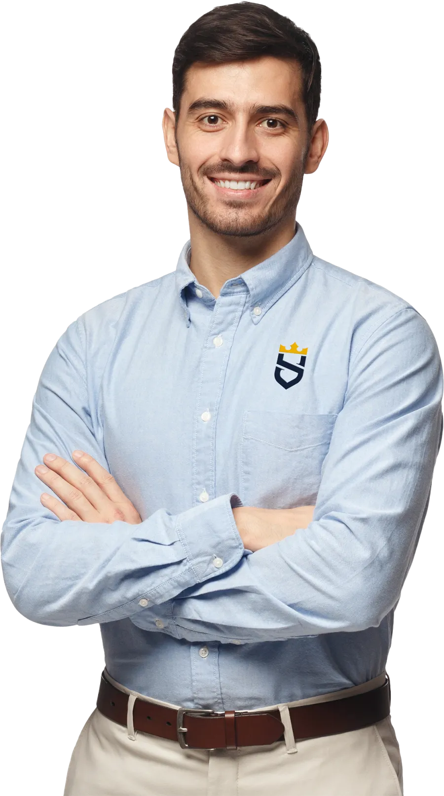 Smiling man in light blue button-up shirt with crown logo, beige pants, and brown belt standing with arms crossed.