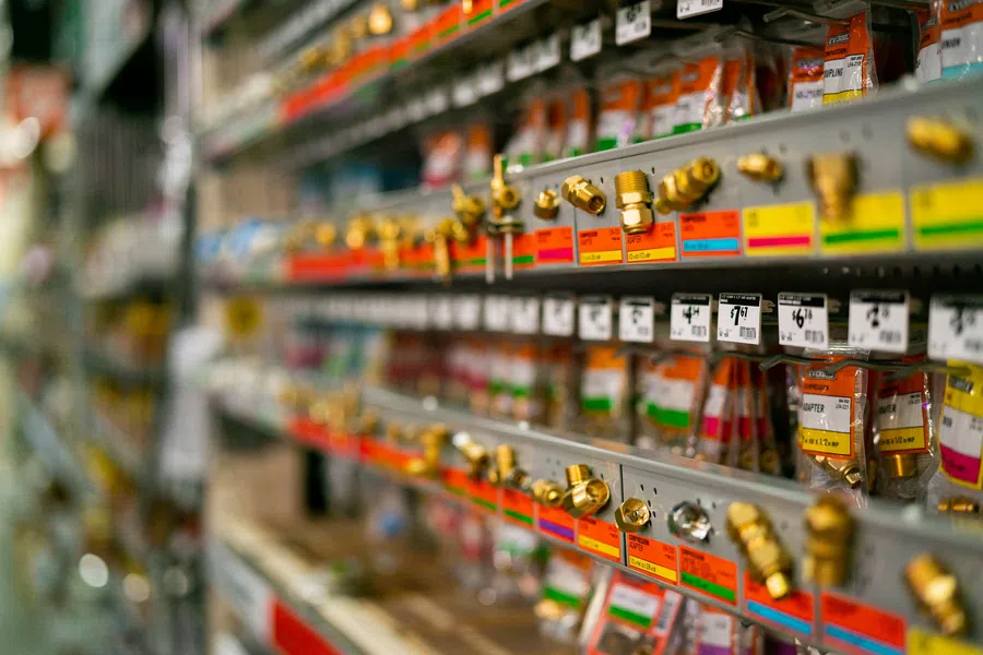 Rows of plumbing fittings and brass connectors organized on store shelves with colorful labels and price tags.