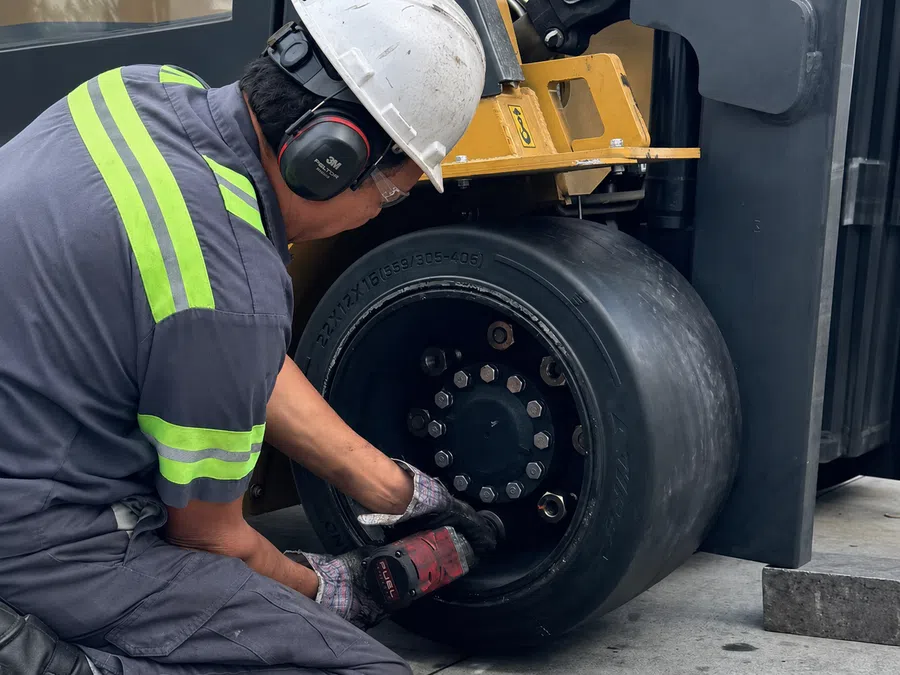Worker in safety gear repairing or maintaining a heavy-duty forklift tire with power tool in industrial setting