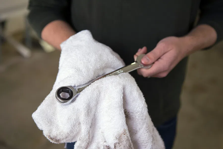 Person cleaning a ratchet wrench with a white cloth, focusing on tool maintenance in a workshop setting.