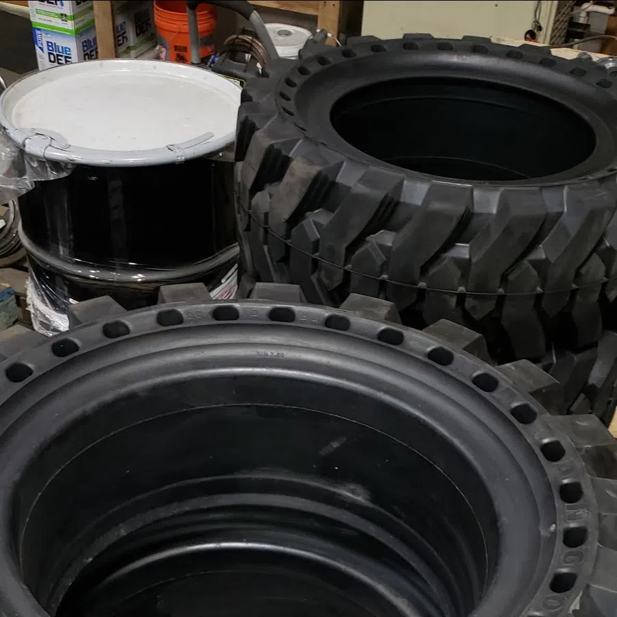 Stacked off-road tires with deep treads resting on a wooden pallet in a workshop setting.