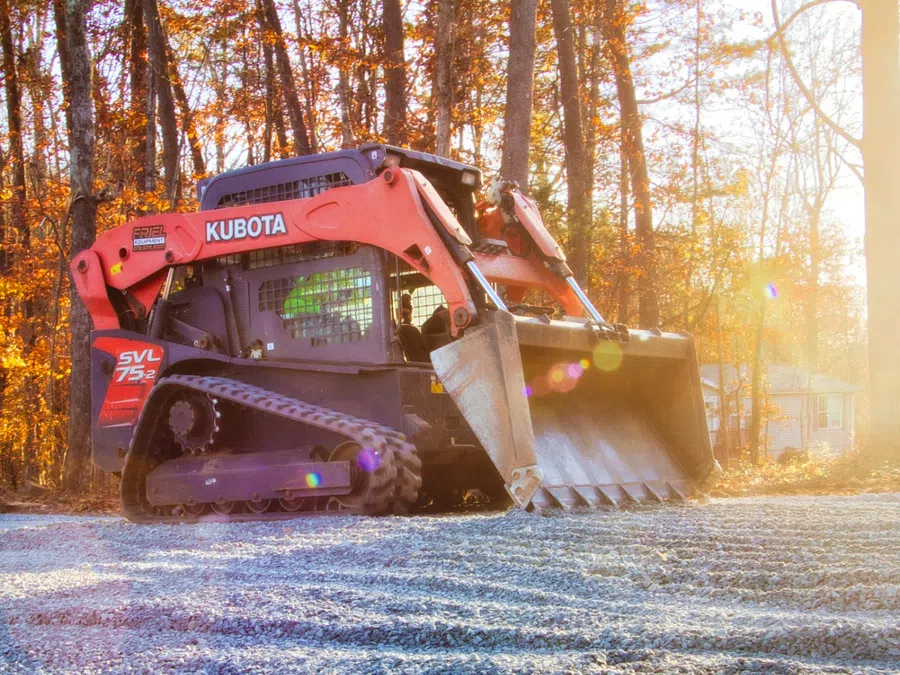 Two red and black forklifts parked side by side on gravel near a building with greenery in the background