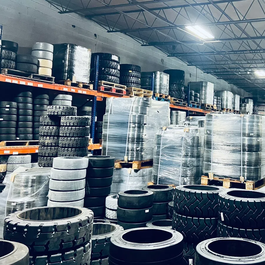 Warehouse filled with stacks of various black tires and pallets wrapped in plastic film on steel shelves.