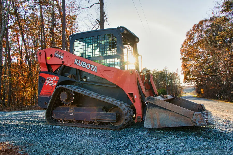 Kubota SVL 75-2 compact track loader on gravel road with sun flare and autumn trees in the background