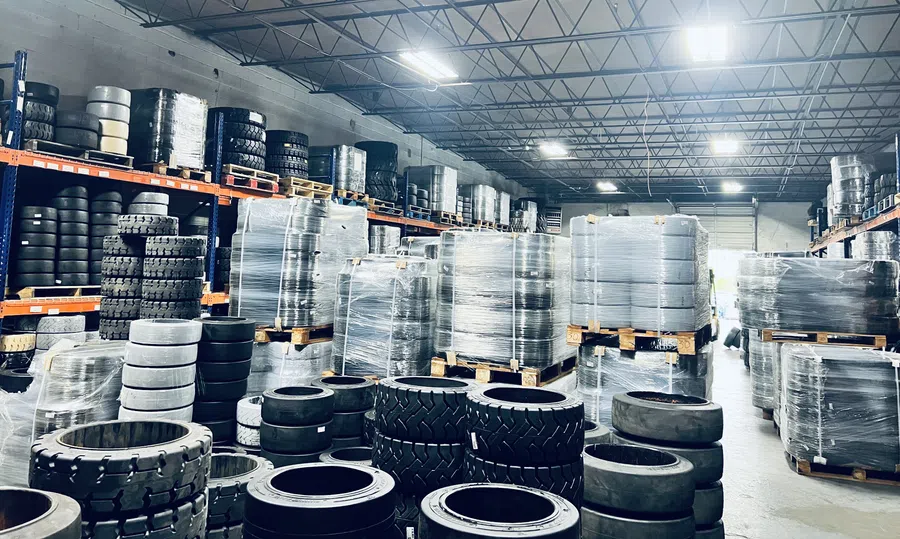 Warehouse filled with stacked and wrapped industrial tires on pallets under bright ceiling lights.