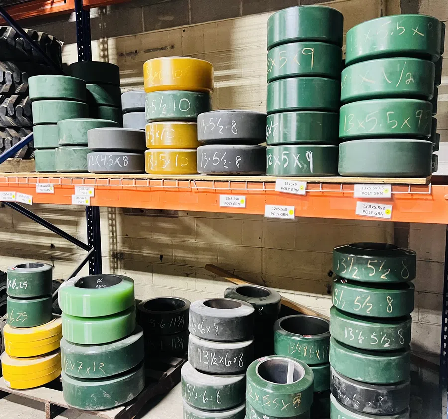 Stacks of green, yellow, and black cylindrical industrial parts with handwritten white measurements on metal shelving.