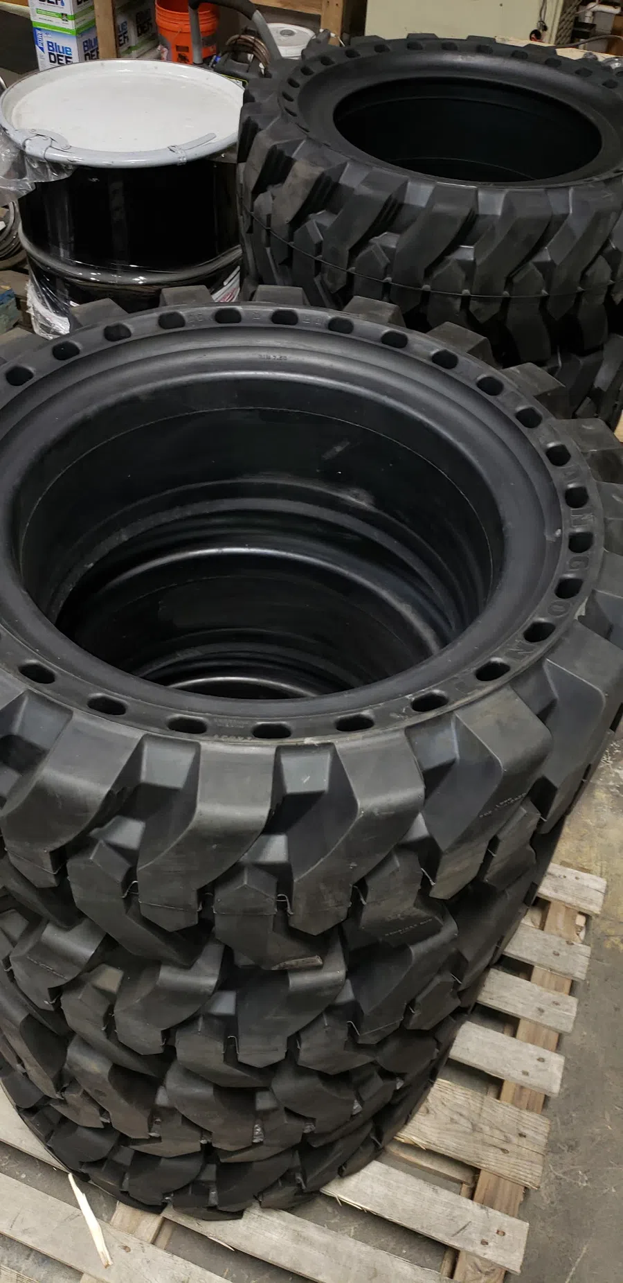 Stacked off-road tires with deep treads resting on a wooden pallet in a workshop setting.