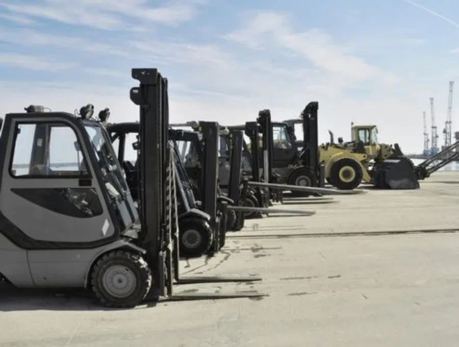 Row of forklifts and heavy machinery parked on an industrial dock under a blue sky