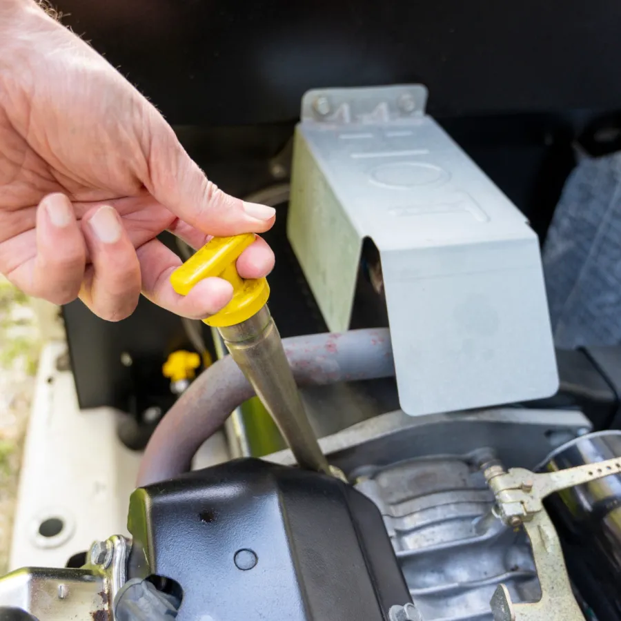 Hand checking oil level in a small engine with a yellow dipstick for maintenance.