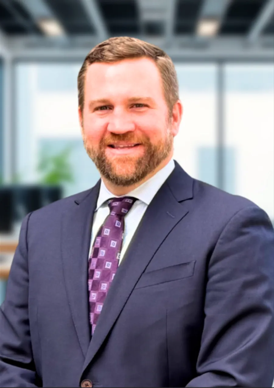Smiling man with beard in navy suit and patterned purple tie in modern office setting.