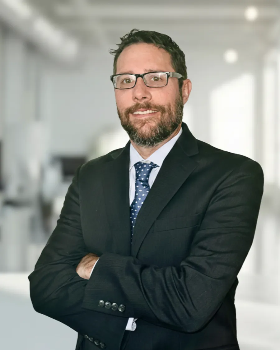 Professional man with beard and glasses wearing a dark suit and blue polka dot tie in an office.