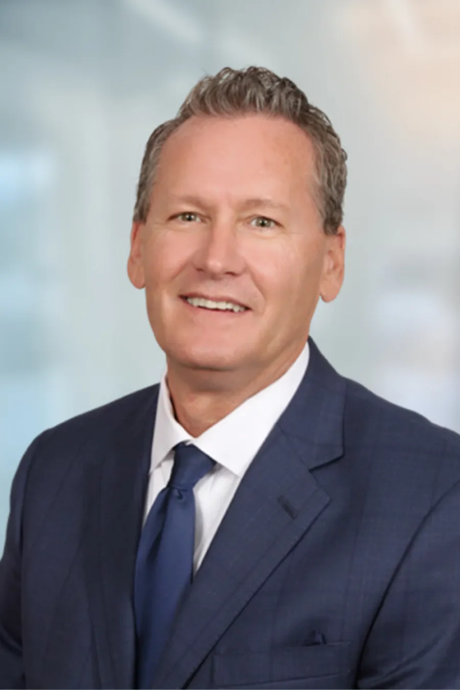 Smiling middle-aged man in a navy suit and tie with a blurred office background.