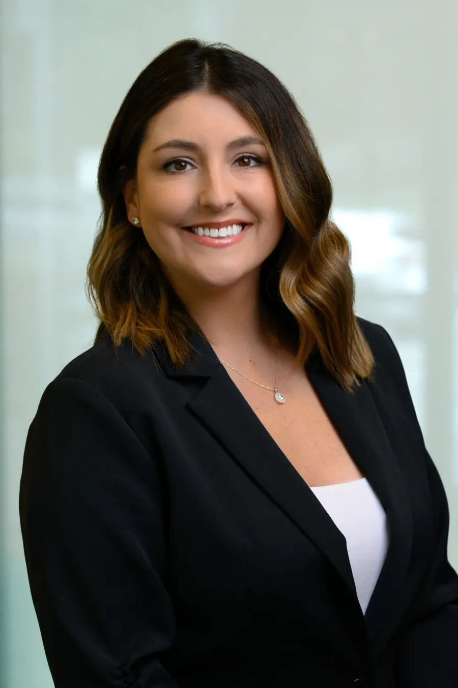 Professional woman with shoulder-length brown hair wearing a black blazer and white top smiling against a light background