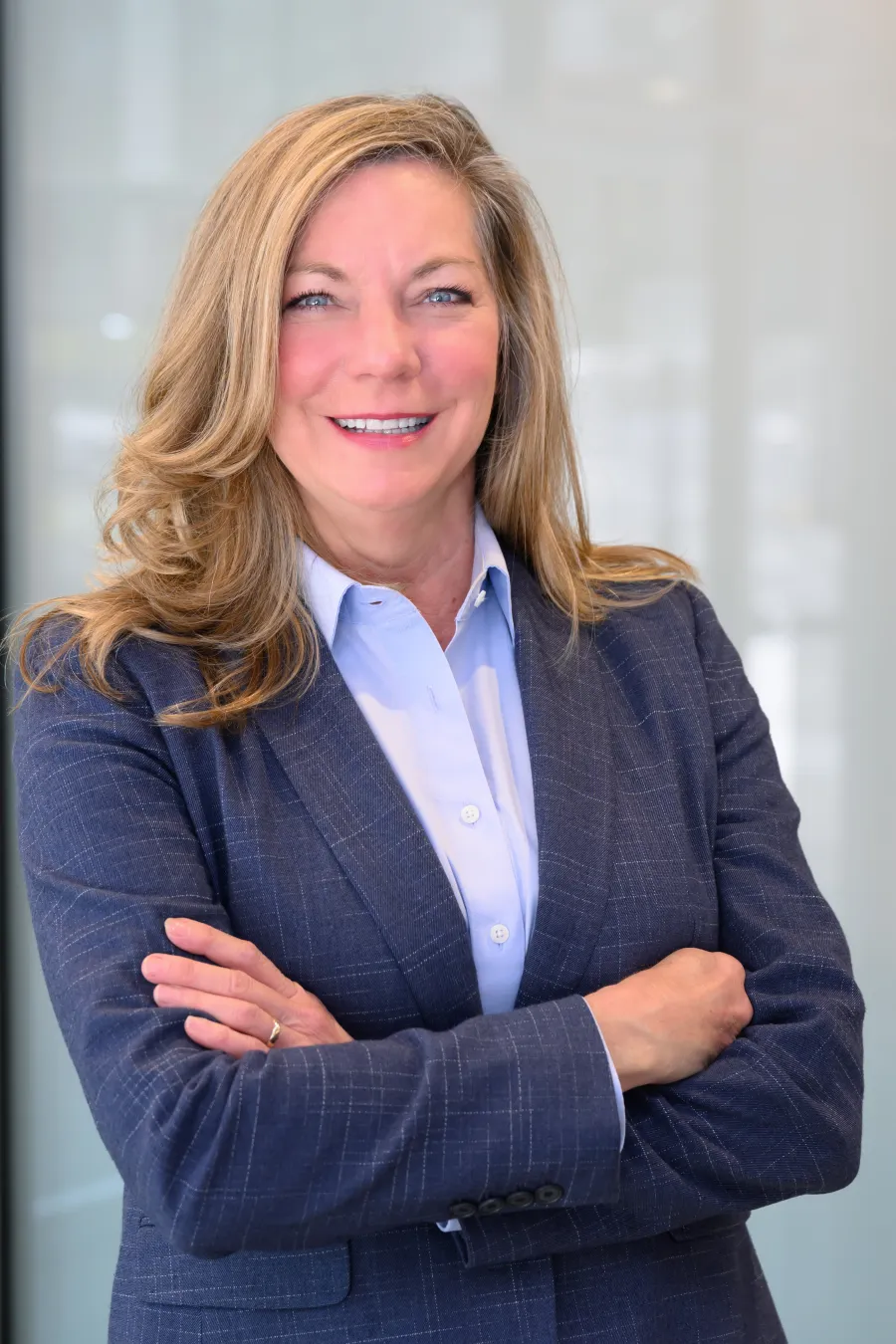 Smiling professional woman with blonde hair in blue suit jacket and light blue shirt posing confidently indoors.