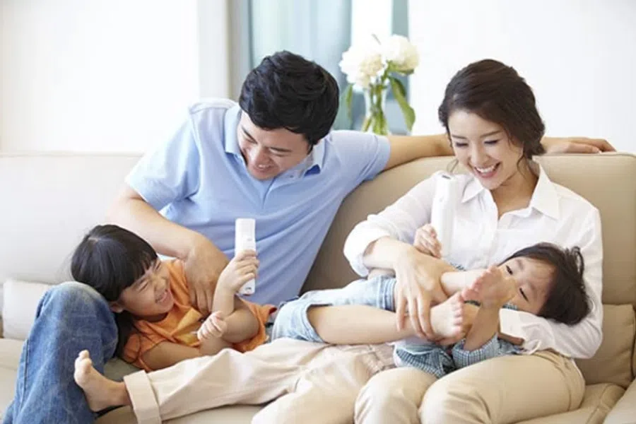 Happy Asian family with two children playing and laughing together on a living room sofa on a sunny day