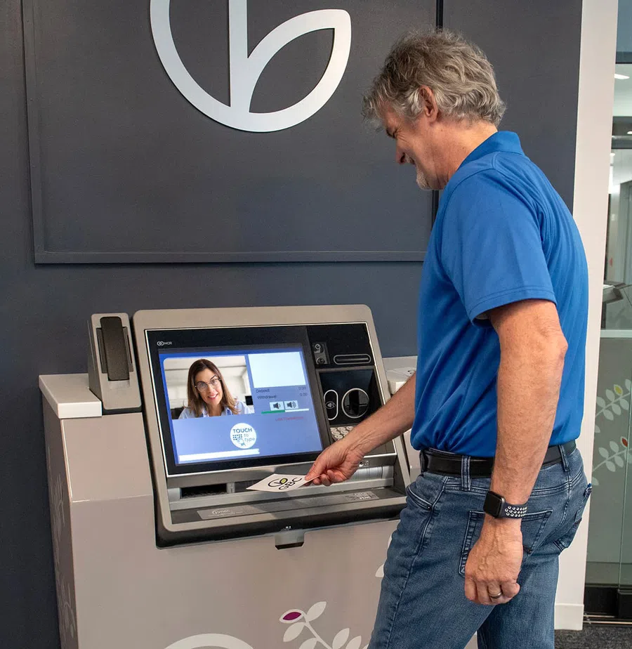 Man using video call kiosk with touchscreen to communicate with woman for remote assistance.