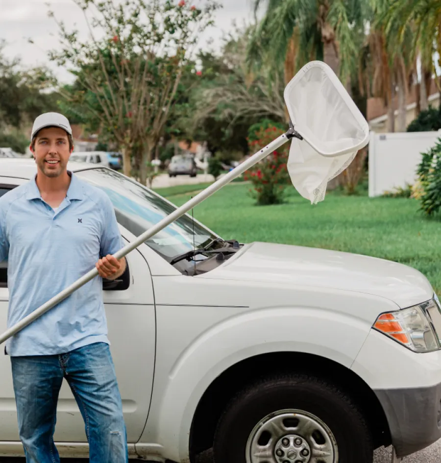 a man holding a pool net next to a car