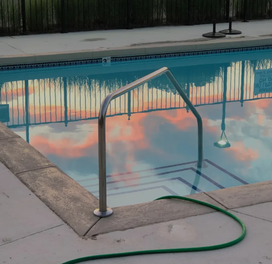 Stainless steel pool handrail reflecting colorful clouds in clear water, surrounded by a clean pool deck.