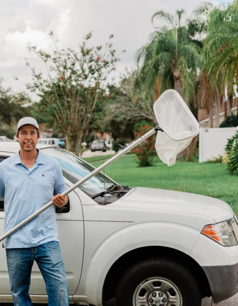a man holding a white pool net next to a car