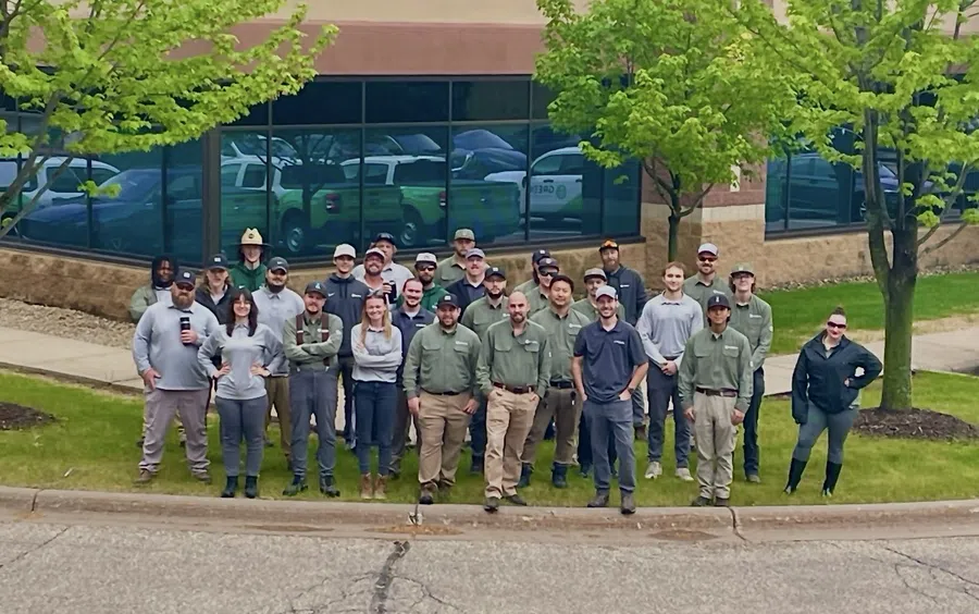 Group of diverse workers standing outside an office building on a grassy area near the street curb