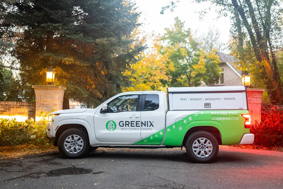 Greenix pest control truck parked by a house with autumn trees and lit lanterns in the background