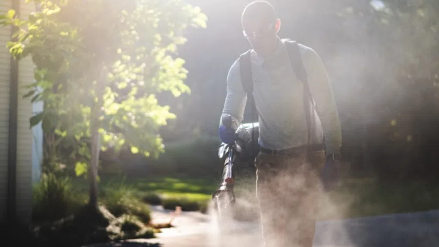 Man wearing backpack sprayer applying mosquito reduction pesticide in a customers yard.