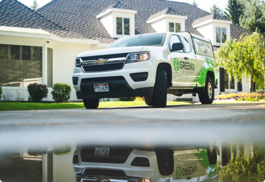 White Greenix service truck parked in front of a house with reflection in water on driveway