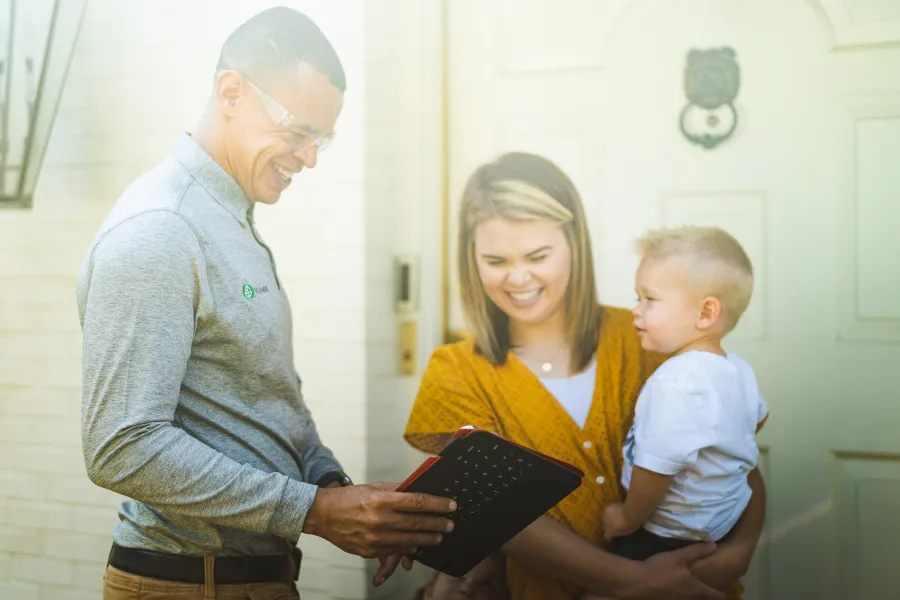 Smiling man showing digital tablet to woman holding child outside home in bright natural light