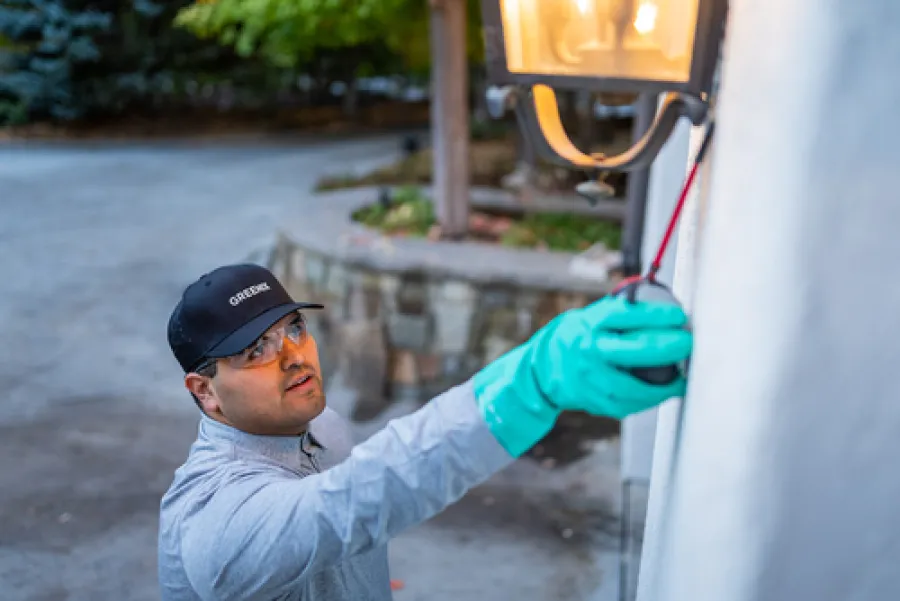 Technician wearing gloves and protective glasses testing an outdoor wall light fixture at dusk