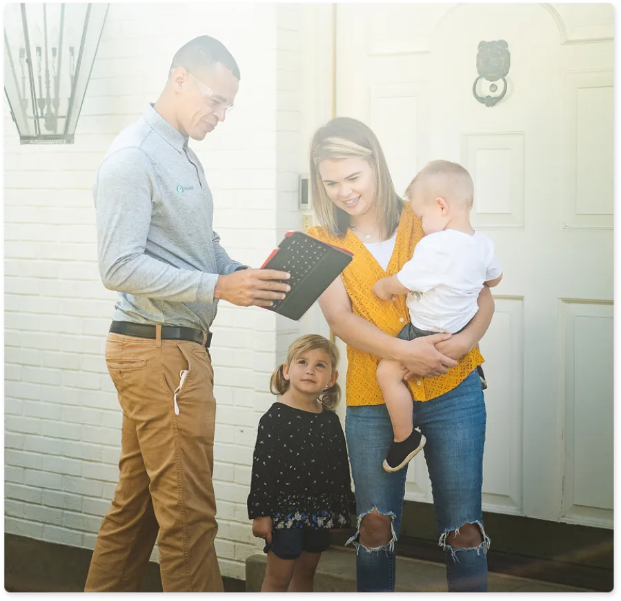 Salesman showing a digital tablet to a mother and her two children outside their home door